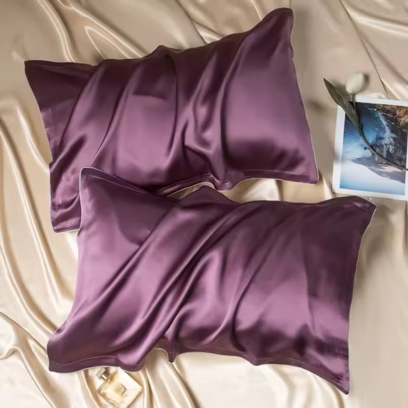 Two deep plum-purple silk pillowcases set on champagne silk fabric with a picture card and perfume.