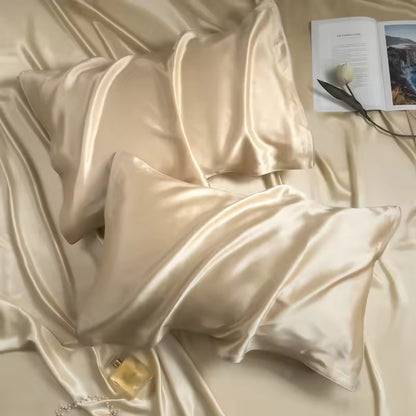 Two champagne gold silk pillowcases laid on matching draped silk with an open book and perfume bottle.
