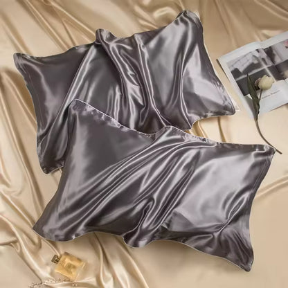 Two dark gray silk pillowcases resting on champagne silk fabric with an open magazine and perfume.