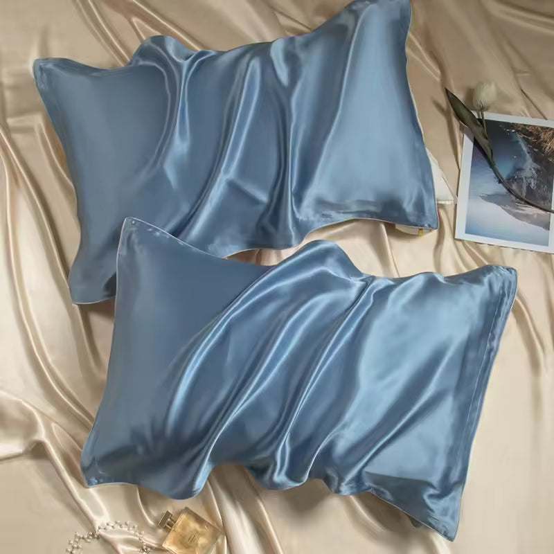 Two light blue silk pillowcases set on champagne silk fabric with a picture card and perfume bottle.