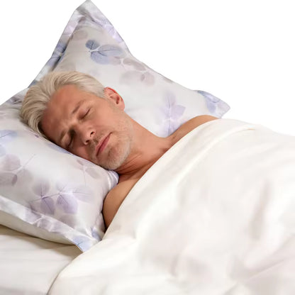 Man with blonde-gray hair sleeping peacefully on a silk leaf-patterned pillowcase in bed.