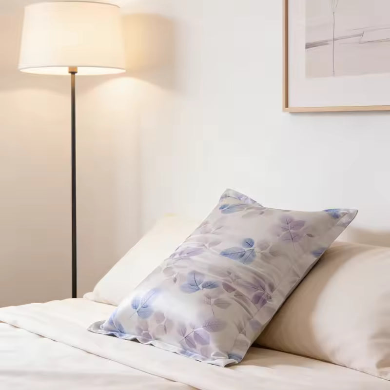 Silk pillowcase with a purple leaf print resting on a bed next to a floor lamp.