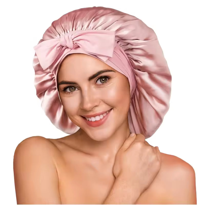 Woman wearing a pink silk sleep bonnet with a front bow detail against a white background.