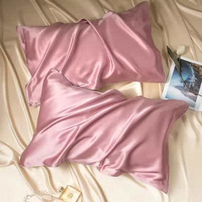 Two dusty mauve-pink silk pillowcases resting on champagne silk fabric with a picture card and perfume.
