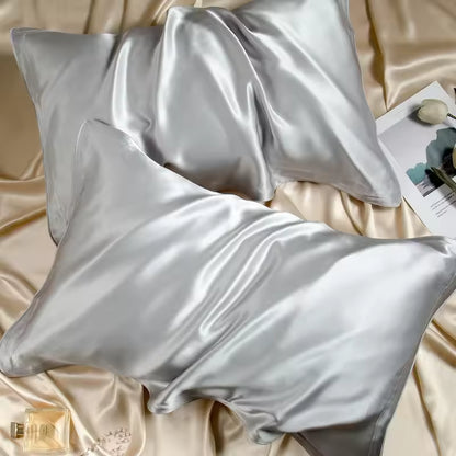 Two silver silk pillowcases on champagne silk fabric with a magazine and perfume bottle.