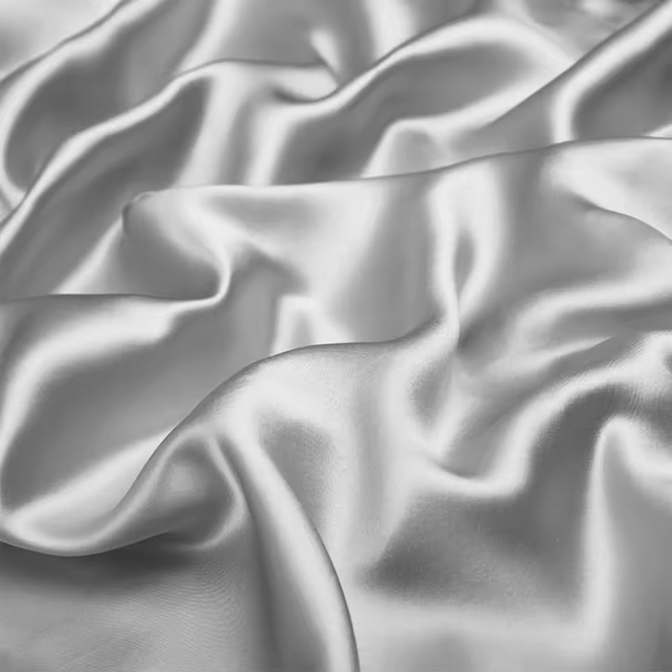 Close-up view of lustrous, rippled silver-white silk fabric with soft waves and shadows.