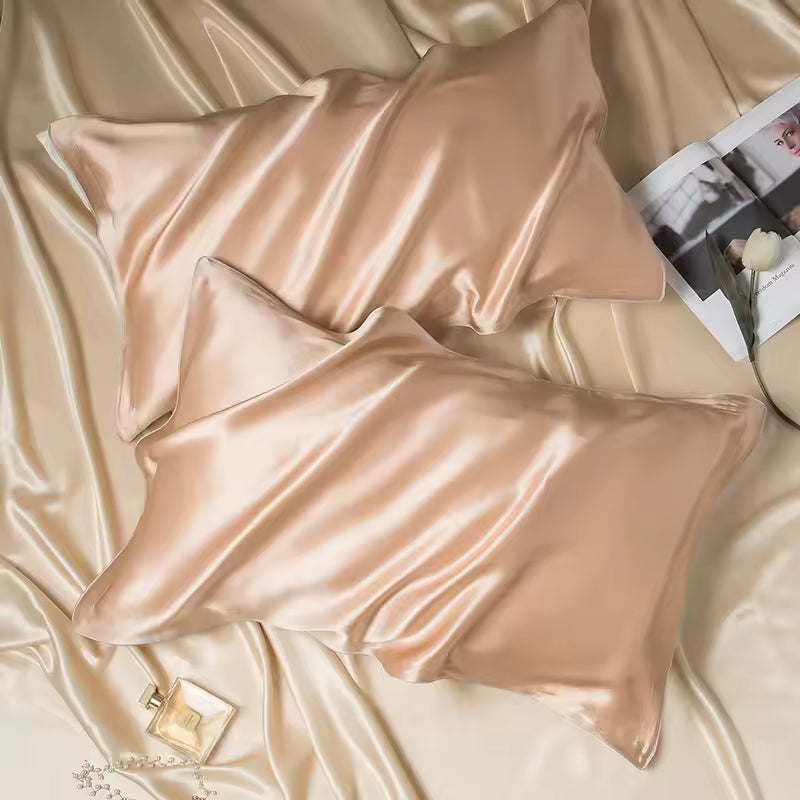 Two golden-champagne silk pillowcases on draped silk fabric with a magazine and perfume bottle.